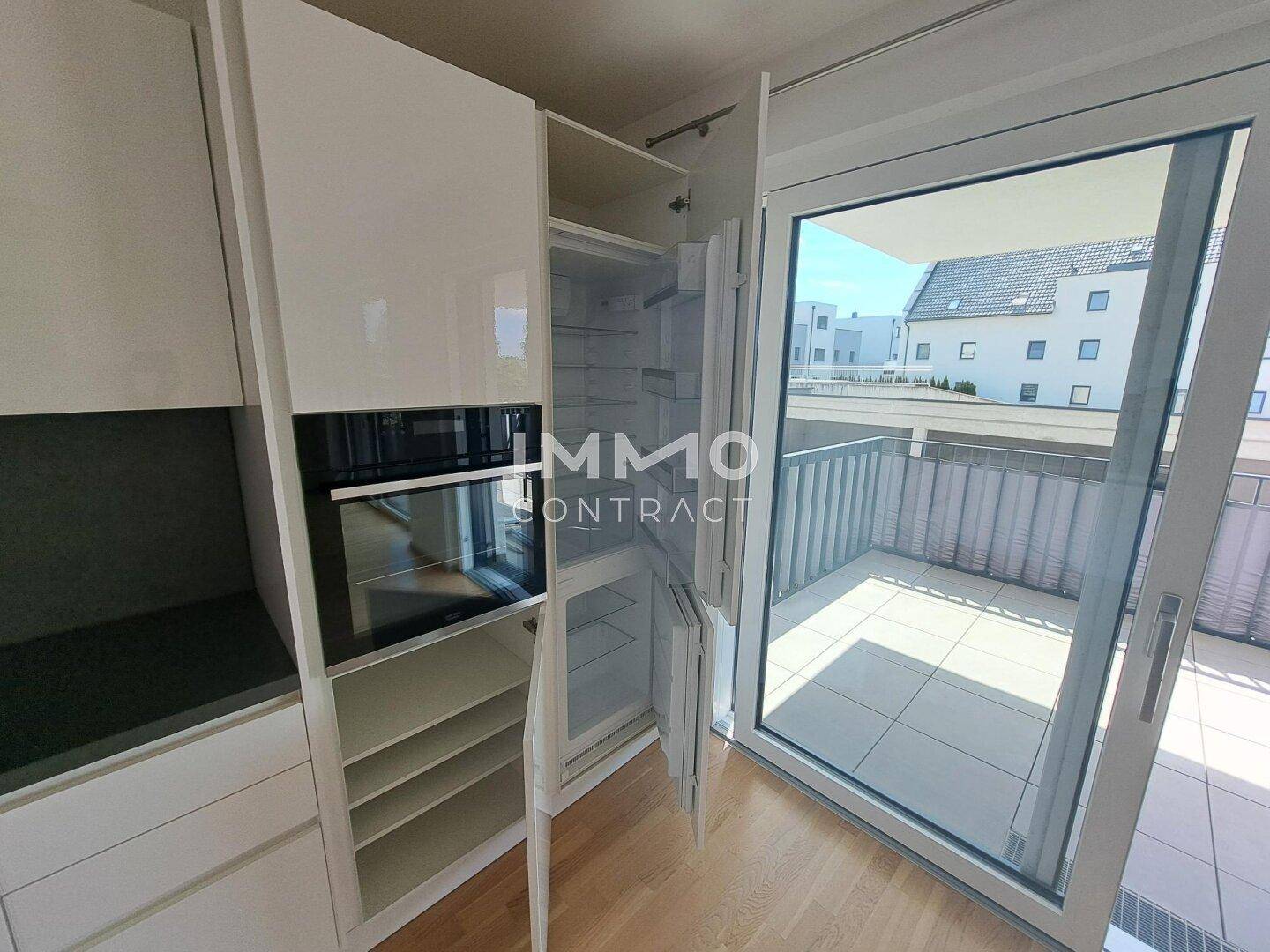 Küchenbereich mit integriertem Kühlschrank und Backofen, sowie großem Zugang zur Terrasse.