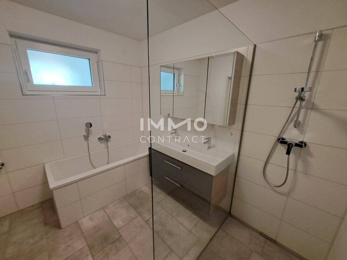 Modernes Badezimmer mit Badewanne, Doppelwaschbecken, Spiegelschrank und Fenster.
