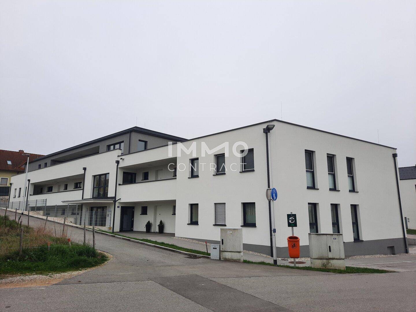 Modernes Mehrfamilienhaus mit weißer Fassade, dunklen Fenstern und klaren Linien.