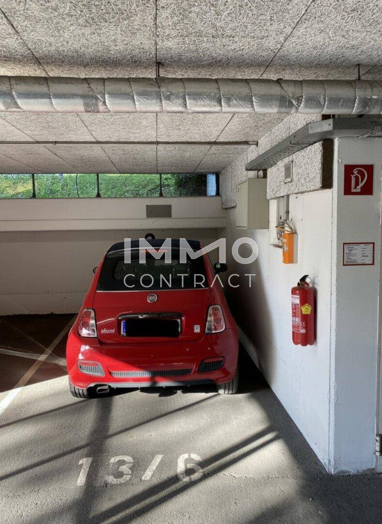 Rückansicht eines roten Autos auf einem Tiefgaragenstellplatz mit Betonboden und Deckenstrukturen.