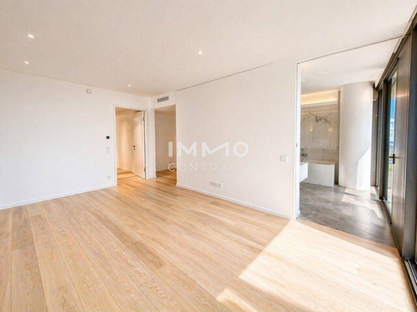 Heller, leerer Wohnbereich mit Holzboden und Zugang zu einem Badezimmer und Balkon.