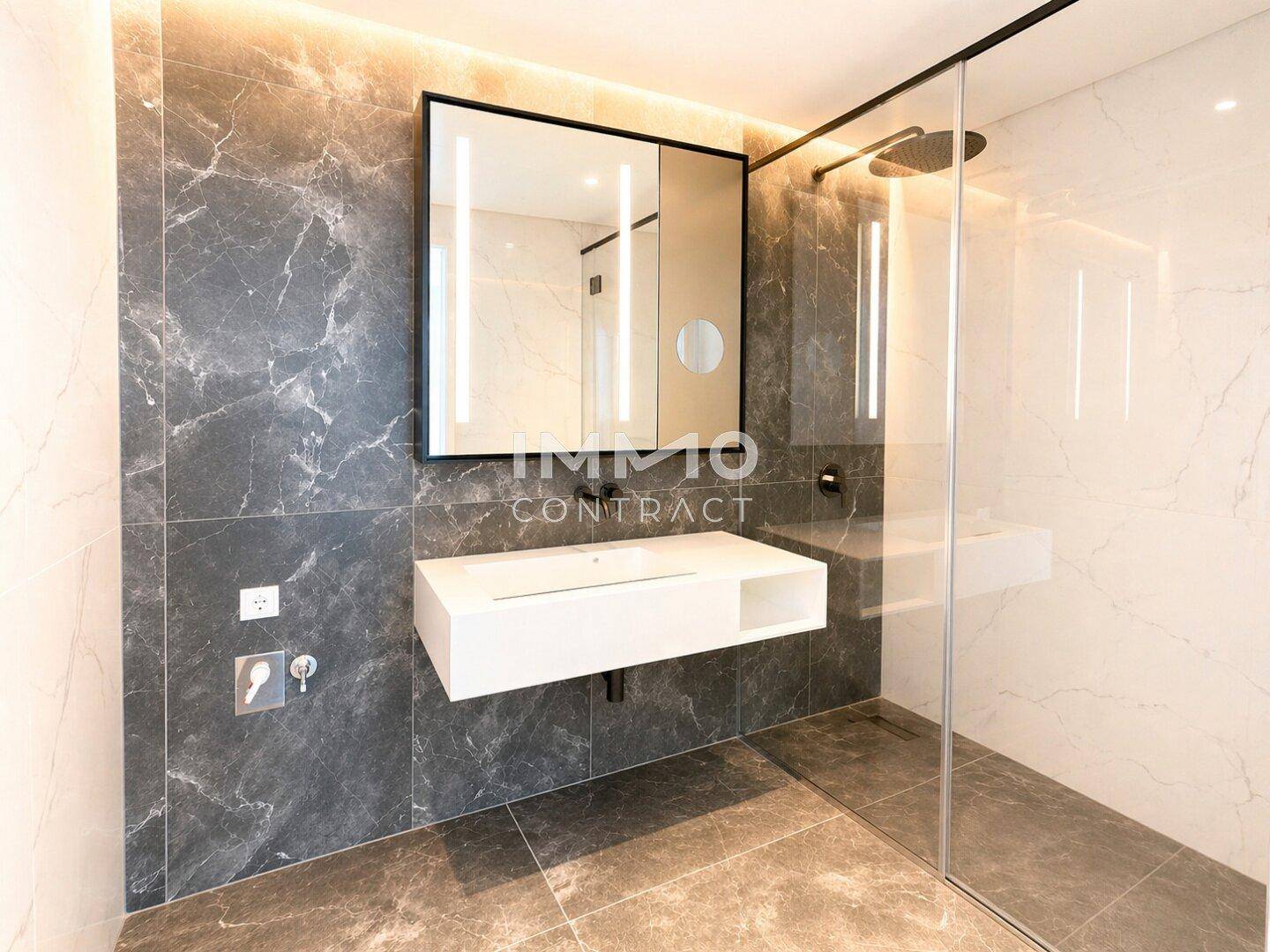 Modernes Badezimmer mit dunklen Marmorfliesen, schwebendem Waschtisch und großer Duschkabine.