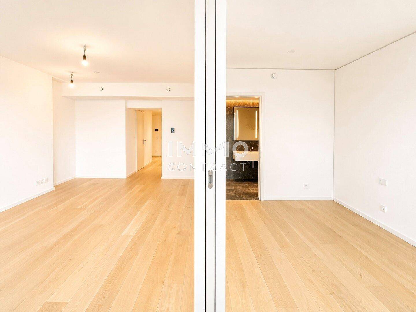 Helles Wohnzimmer mit Holzboden und Blick durch die Glastür in einen weiteren Raum.