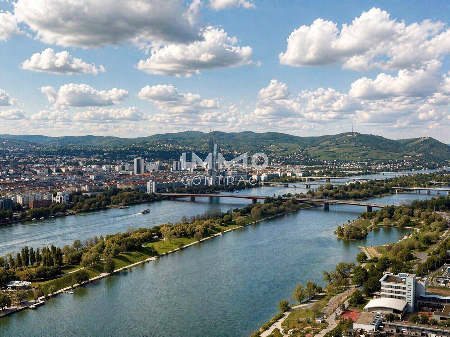 Panoramablick auf die Stadt mit dem Fluss und den umliegenden Bergen unter einem blauen Himmel.