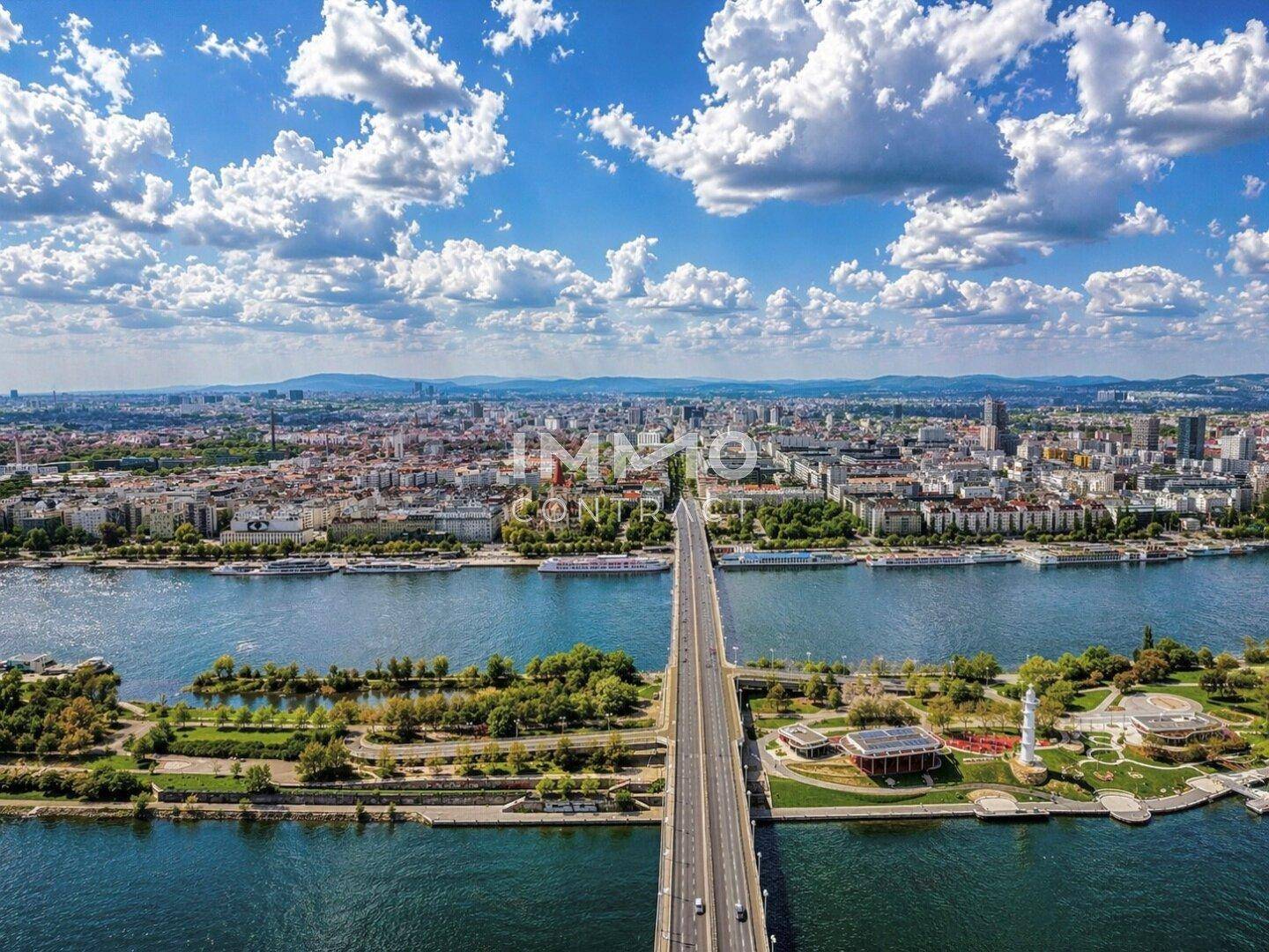 Luftaufnahme der Stadt mit einer langen Brücke über den Fluss und umliegenden Grünflächen.