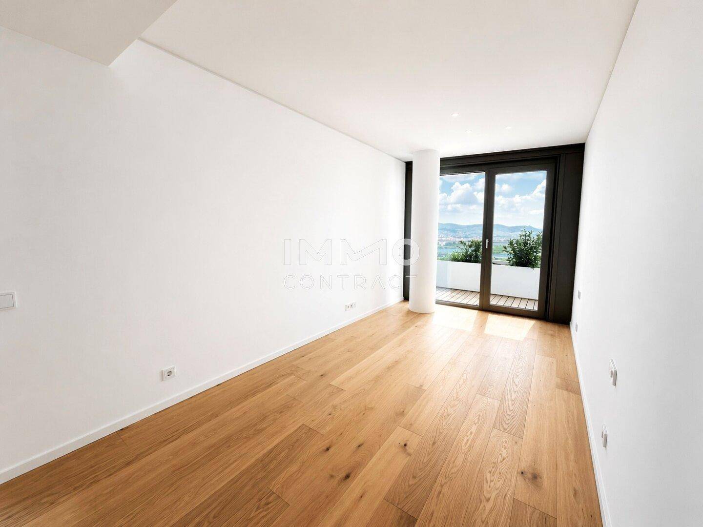 Helles Schlafzimmer mit Holzboden und Zugang zu einem Balkon, der einen grünen Ausblick bietet.