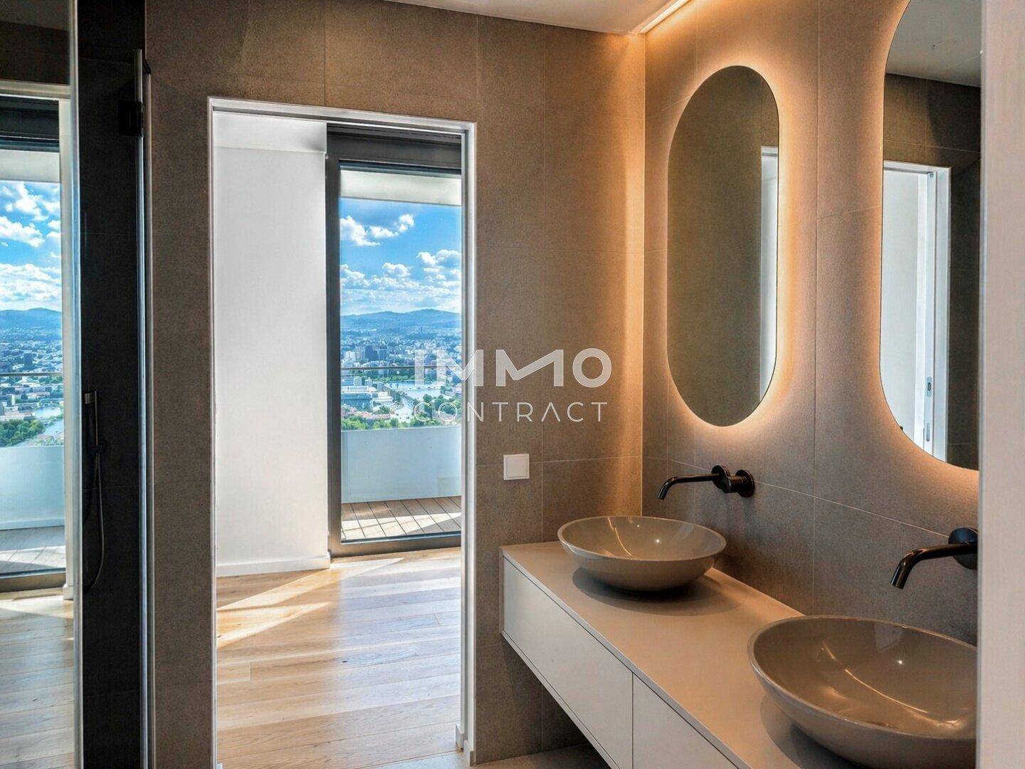 Modernes Badezimmer mit Doppelwaschbecken und beleuchteten Spiegeln, verbunden mit einem hellen Raum.