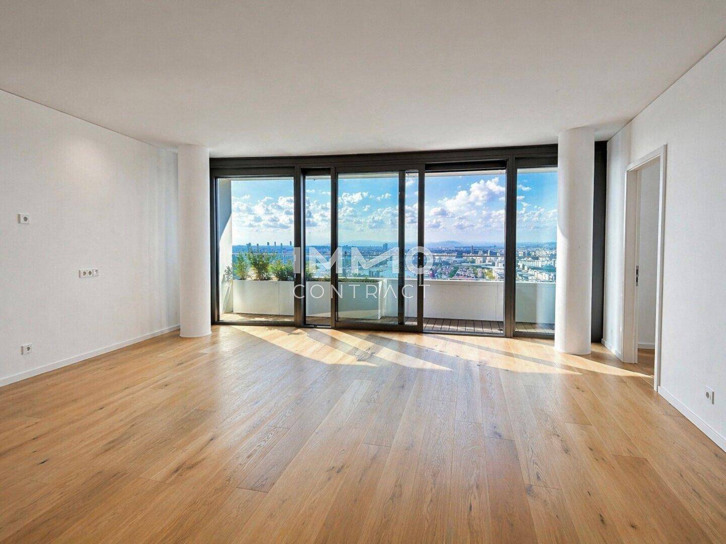 Geräumiges Wohnzimmer mit Holzboden und großen Fenstern, die einen Panoramablick auf die Stadt ermöglichen.