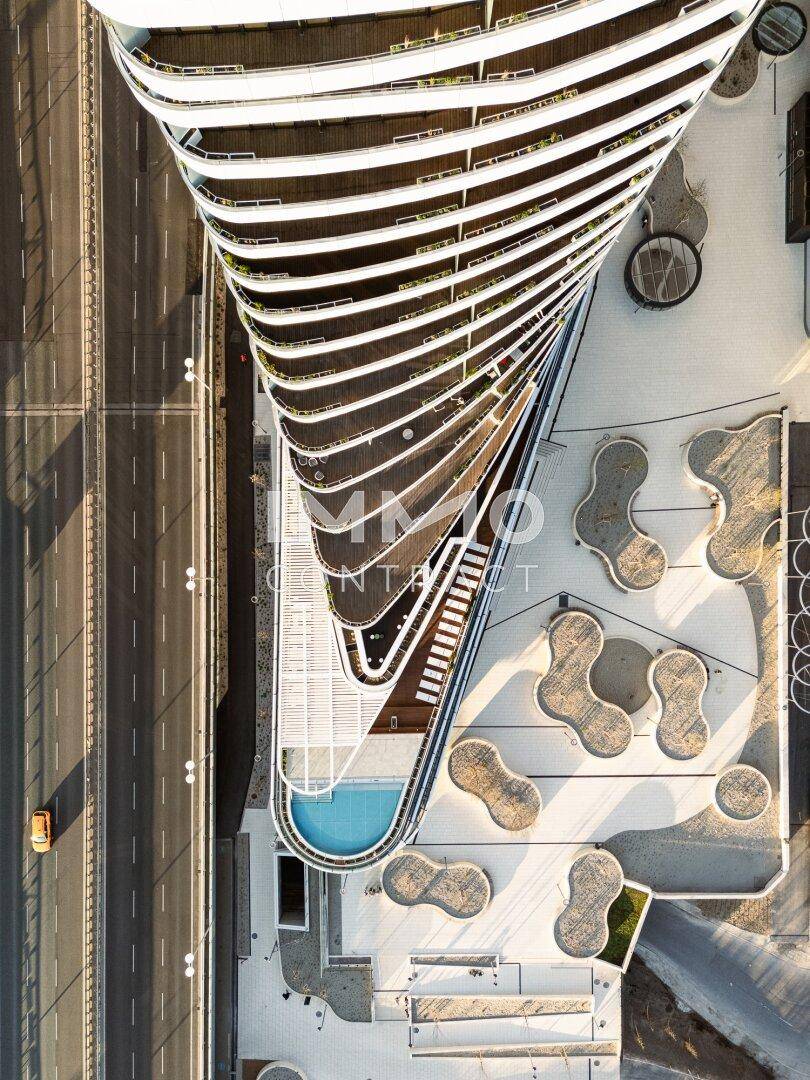 Architektonisch beeindruckendes Gebäude mit geschwungenen Balkonen und einem Poolbereich von oben gesehen.