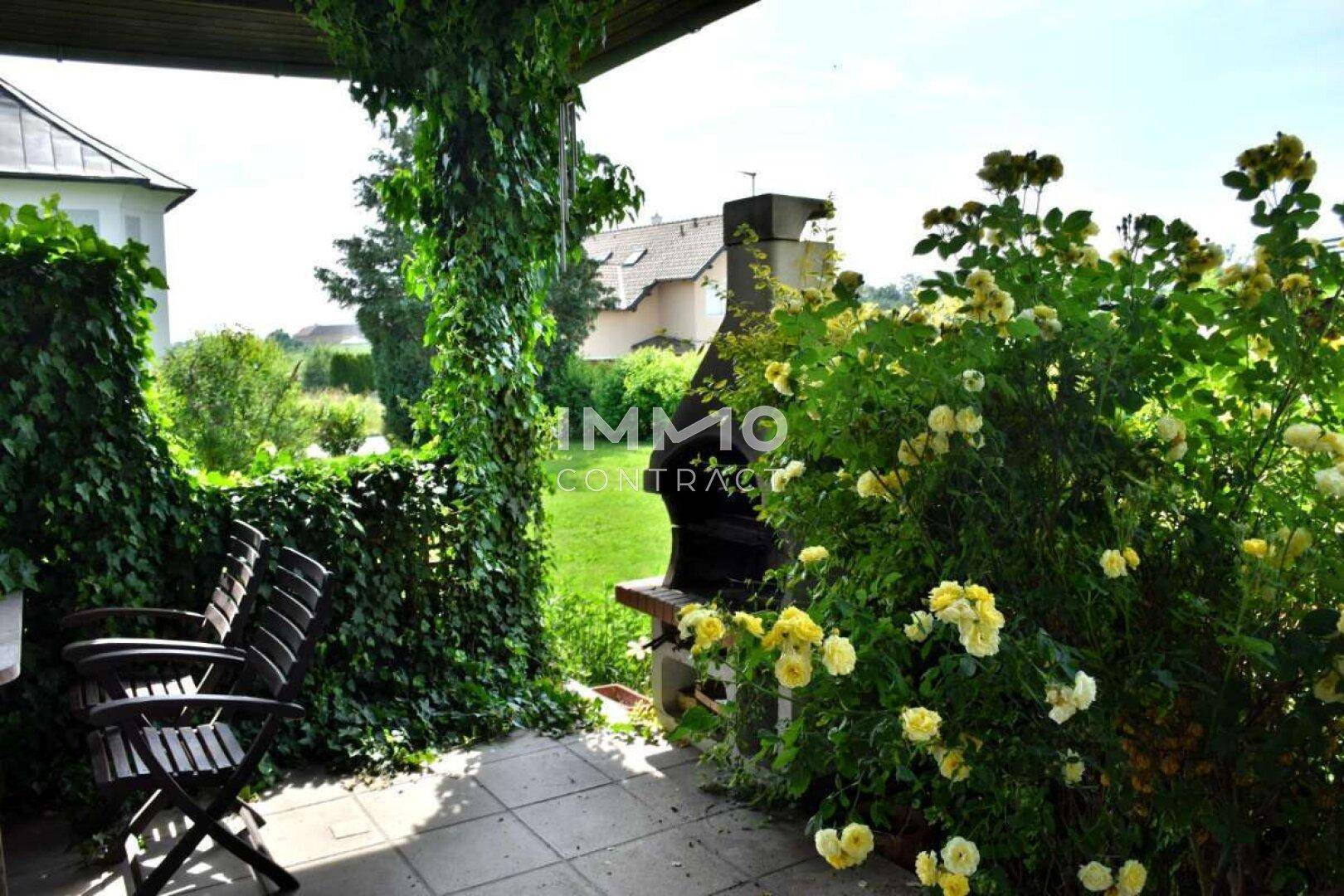 Überdachte Terrasse mit integriertem Grillplatz und üppiger Begrünung, ideal für Mahlzeiten im Freien.