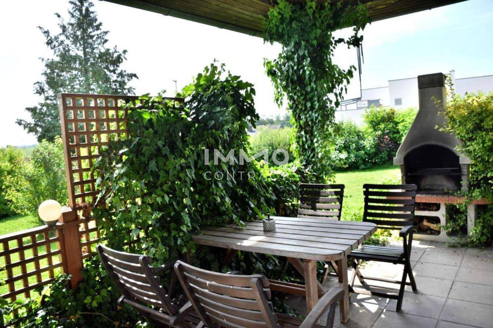 Gemütlicher Essbereich auf der Terrasse mit Holztisch, Stühlen und einem gemauerten Grill im Grünen.