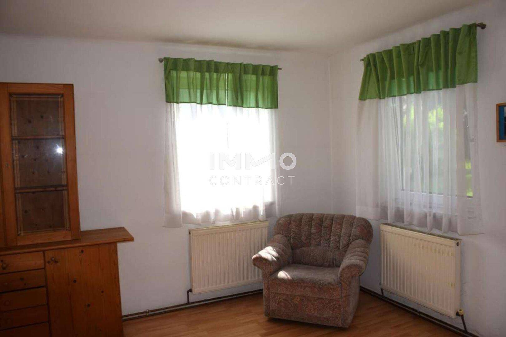 Gemütlicher Raum mit Parkettboden, zwei Fenstern und einem Sessel, ideal als Lese- oder Arbeitszimmer.