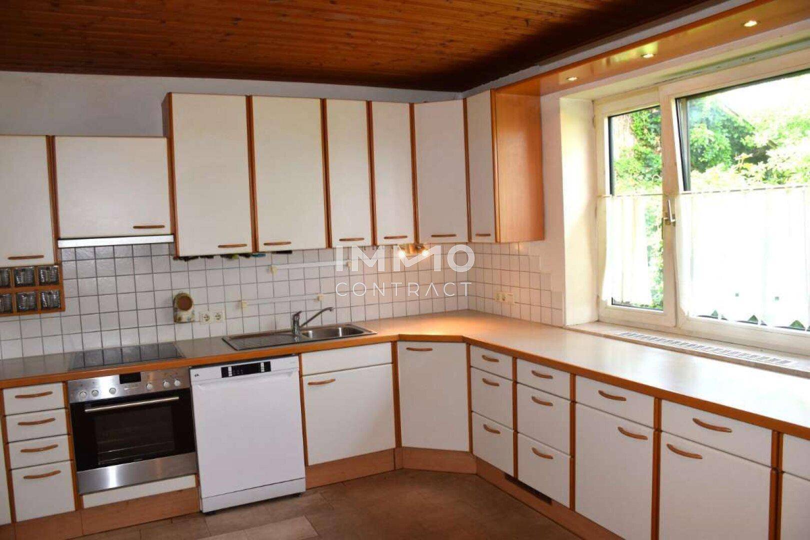 Funktionale Küche mit weißen Schränken, Holzdecke und Fenster mit Blick ins Grüne.