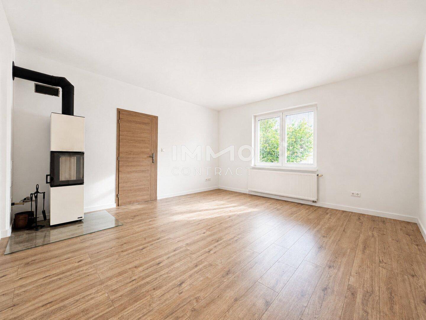 Geräumiges Wohnzimmer mit Kaminofen, Laminatboden und einem Fenster mit Blick ins Grüne.