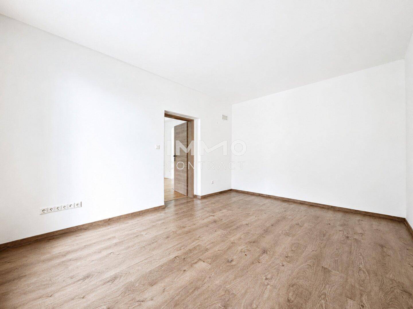 Leerer Raum mit Laminatboden und weißen Wänden, bereit zur individuellen Gestaltung.