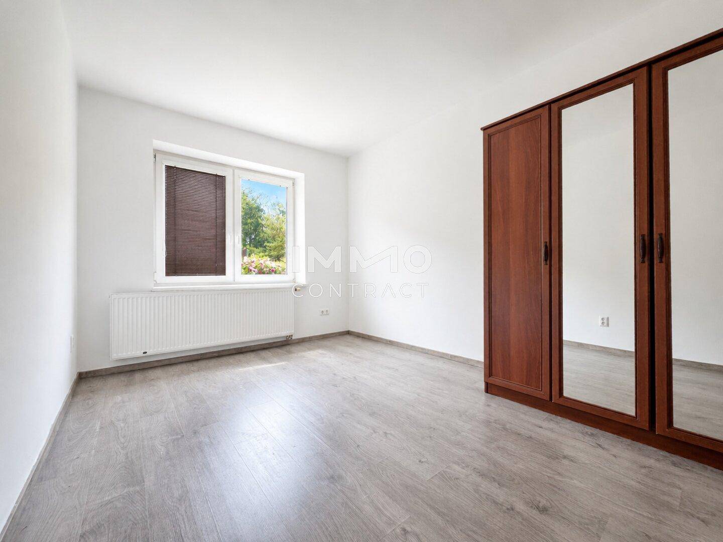 Schlafzimmer mit großem Spiegelschrank, grauem Laminatboden und Fenster für natürliches Licht.