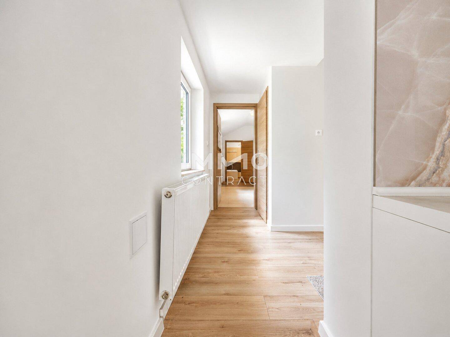 Heller Flur mit Laminatboden, weißen Wänden und einem Fenster für Tageslicht.