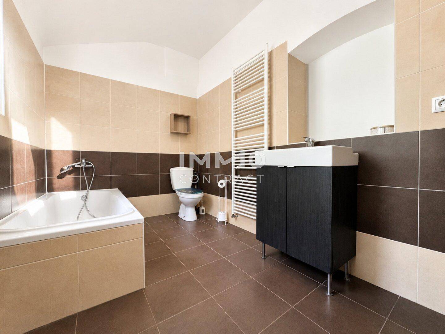 Badezimmer mit Badewanne, WC, Einzelwaschbecken und beheiztem Handtuchhalter in Erdtönen.