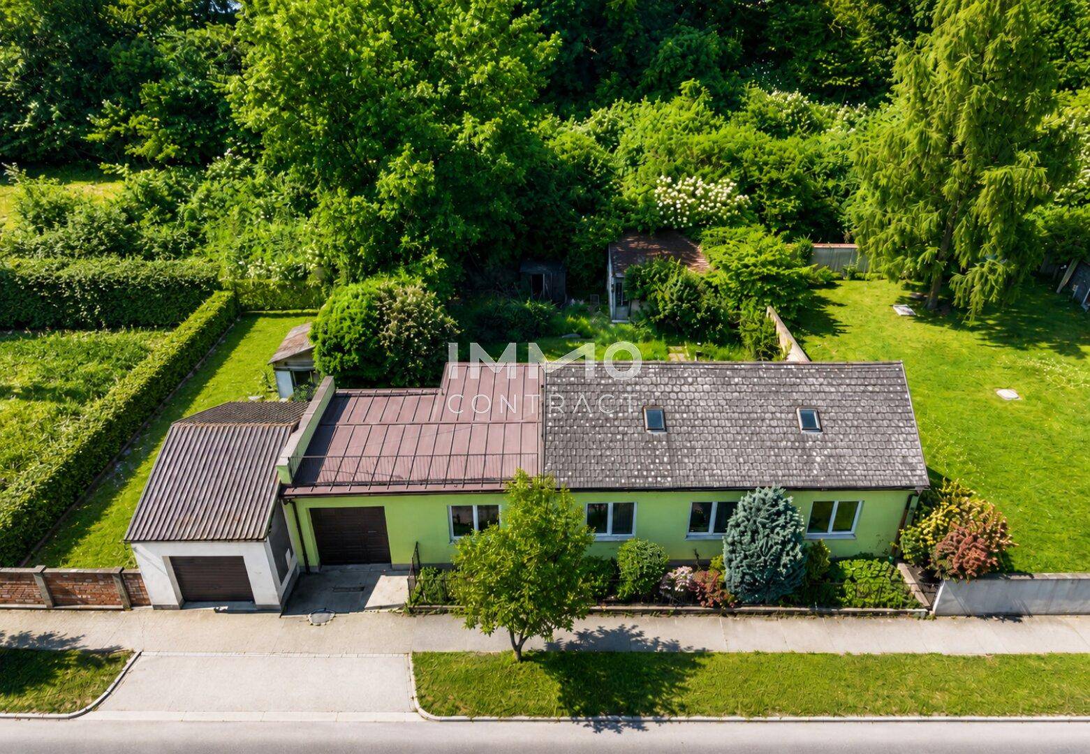 Vogelperspektive des grünen Hauses mit Garage, eingebettet in eine grüne Landschaft.