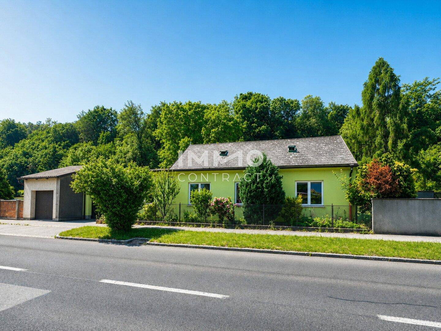 Grünes Einfamilienhaus mit Garage und umgebender Natur, direkt an der Straße gelegen.