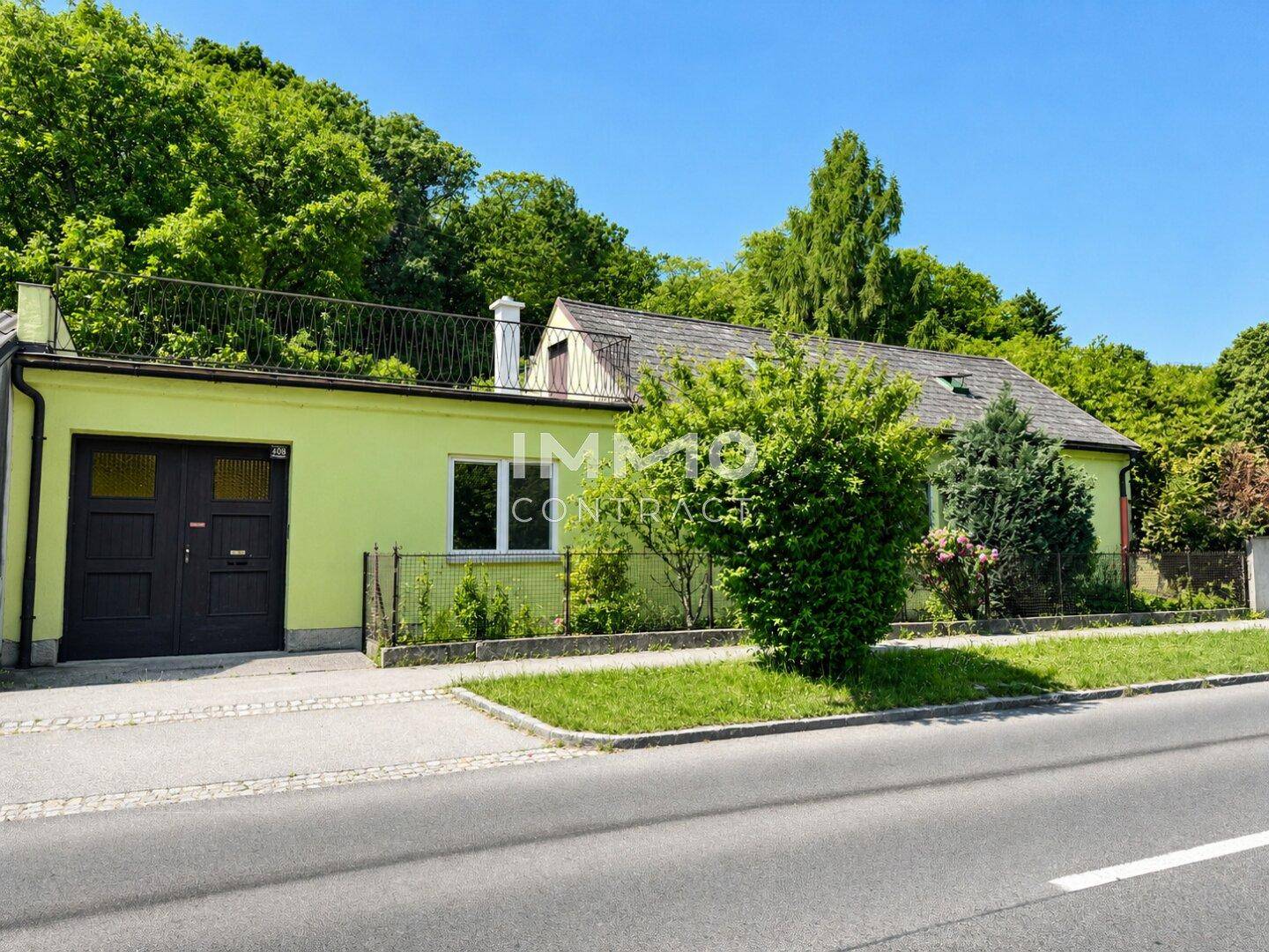 Ansicht des grünen Hauses mit Garage und einer kleinen Dachterrasse darüber.