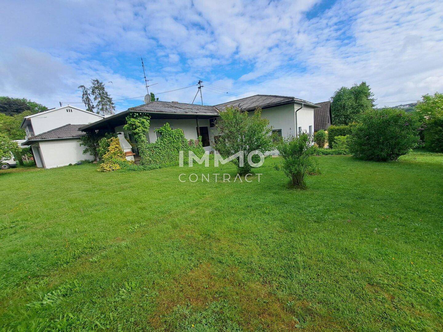 Einfamilienhaus mit großem Garten und grüner Fassadenbegrünung unter bewölktem Himmel.