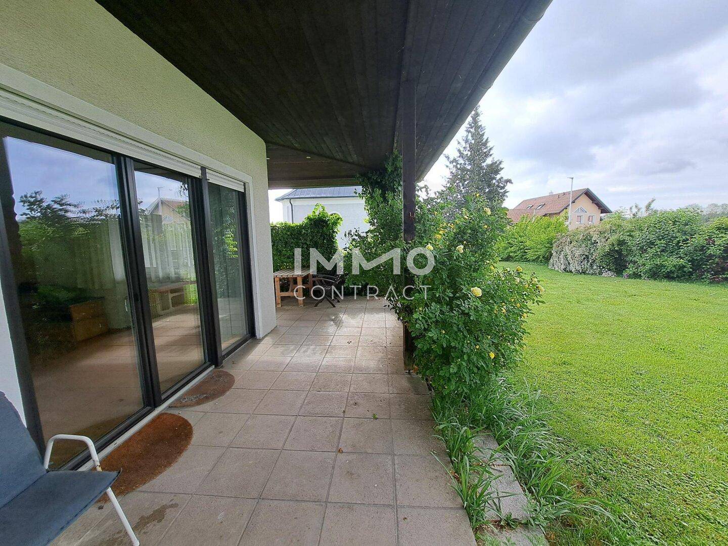 Überdachte Terrasse mit großen Glasschiebetüren zum Haus und Blick auf den grünen Gartenbereich.