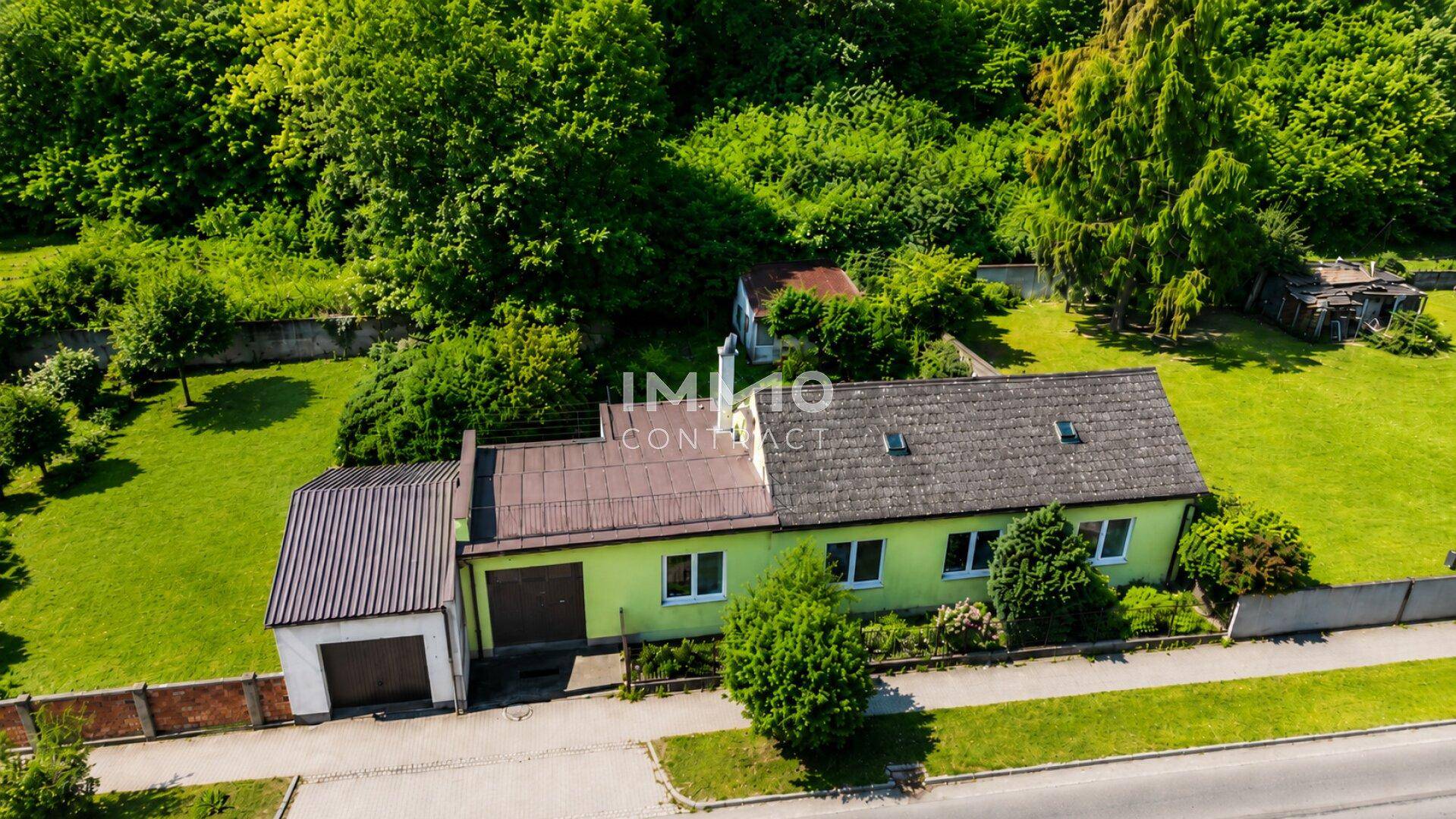 Luftaufnahme des grünen Hauses mit Garage, umgeben von weitläufigen Grünflächen und Bäumen.