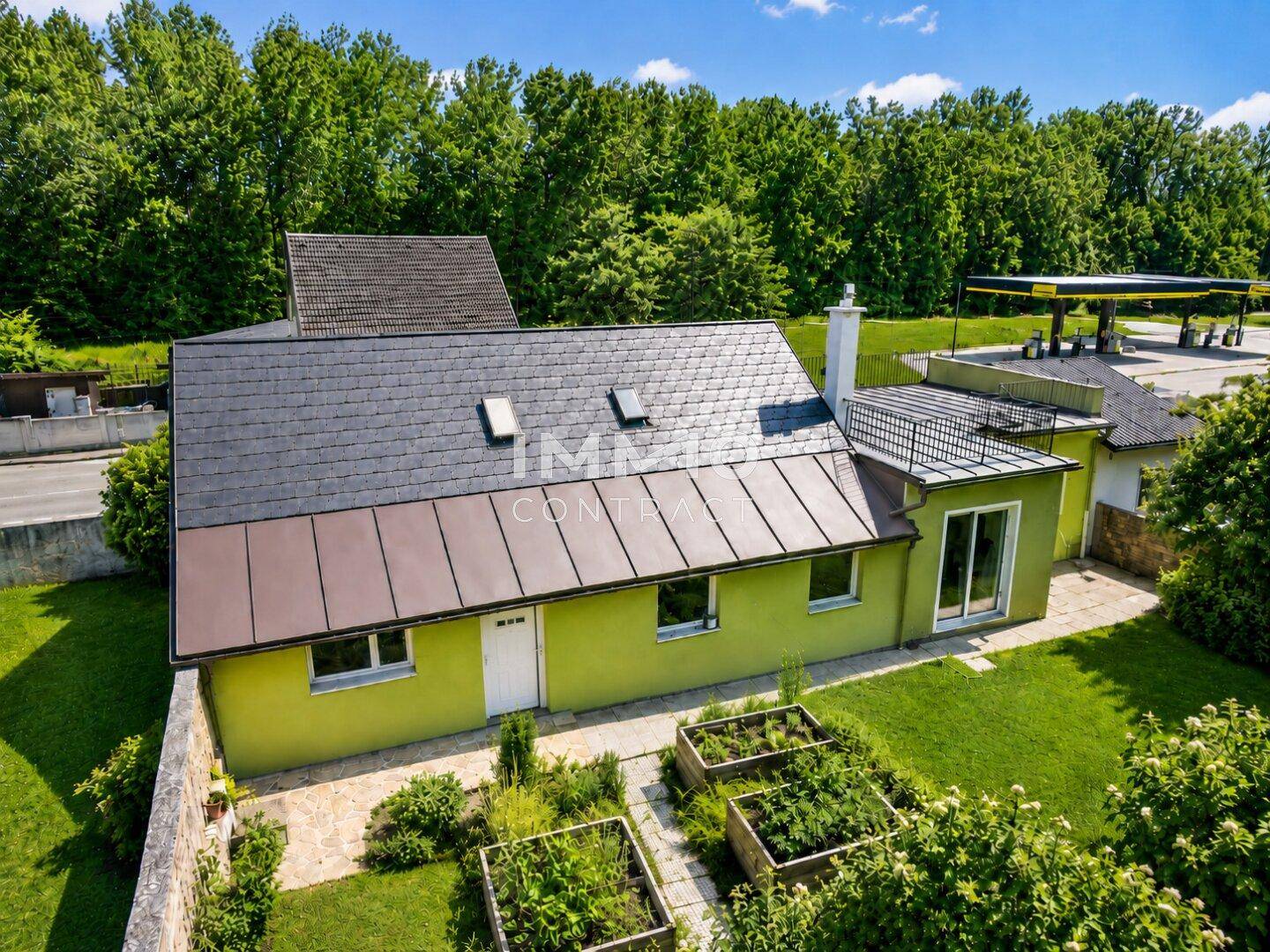 Rückansicht des Hauses mit Gartenbereich, Hochbeeten und einer Dachterrasse.