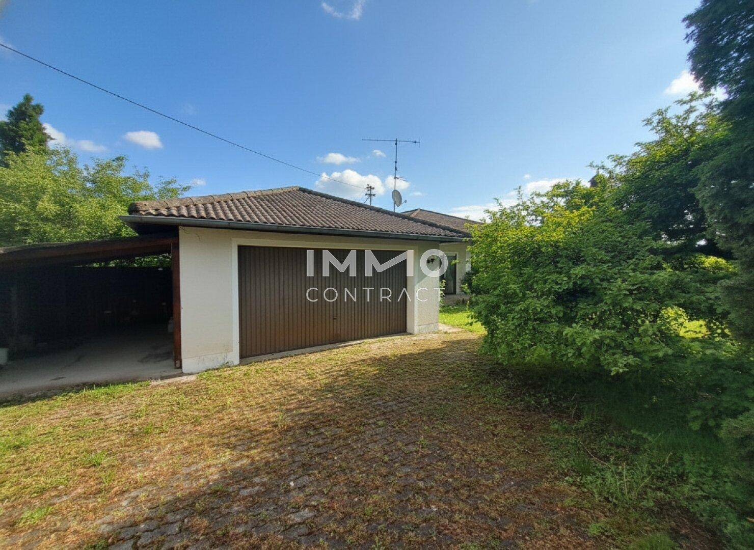 Garage mit braunem Tor und angrenzendem Carport, umgeben von Rasen und Bäumen.