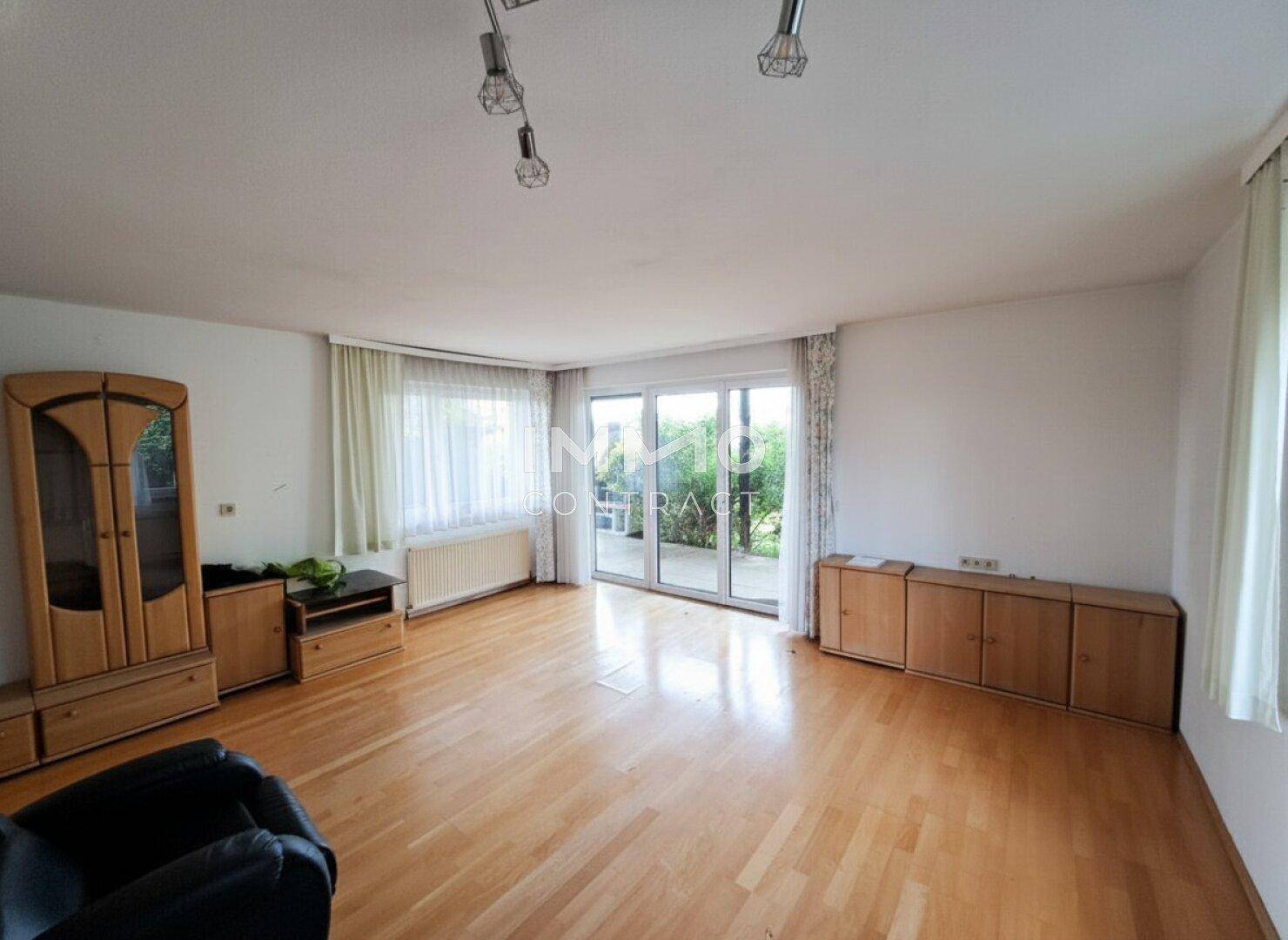 Geräumiges Wohnzimmer mit hellem Parkettboden und viel Tageslicht durch große Fenster.