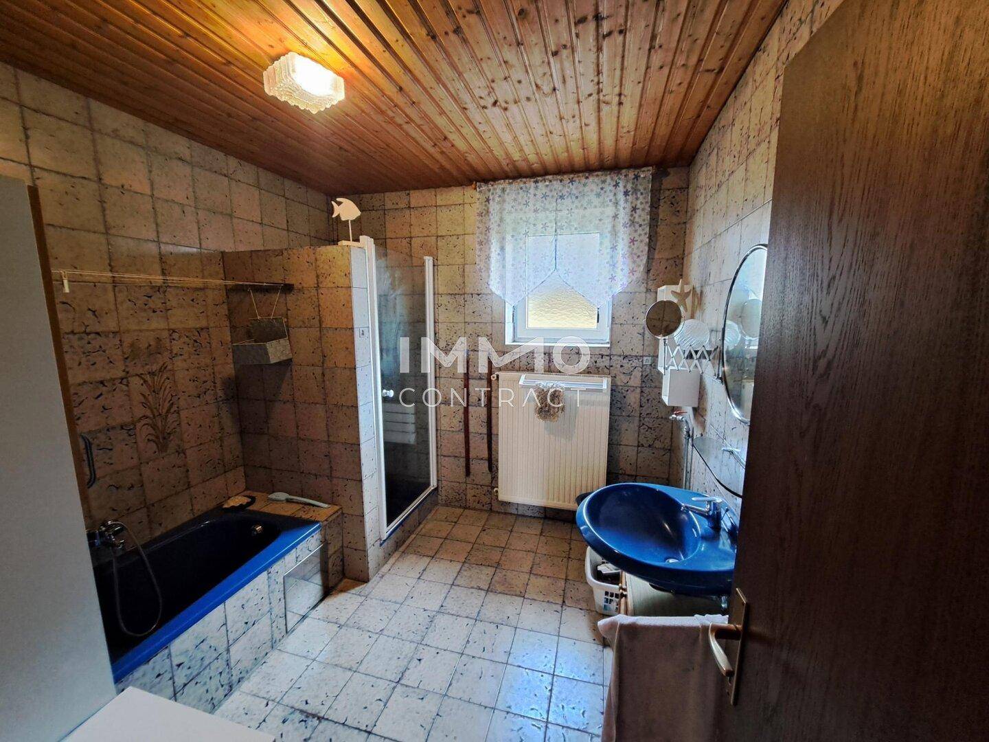 Badezimmer mit Fliesen, blauer Badewanne, Duschkabine und einer Holzdecke.