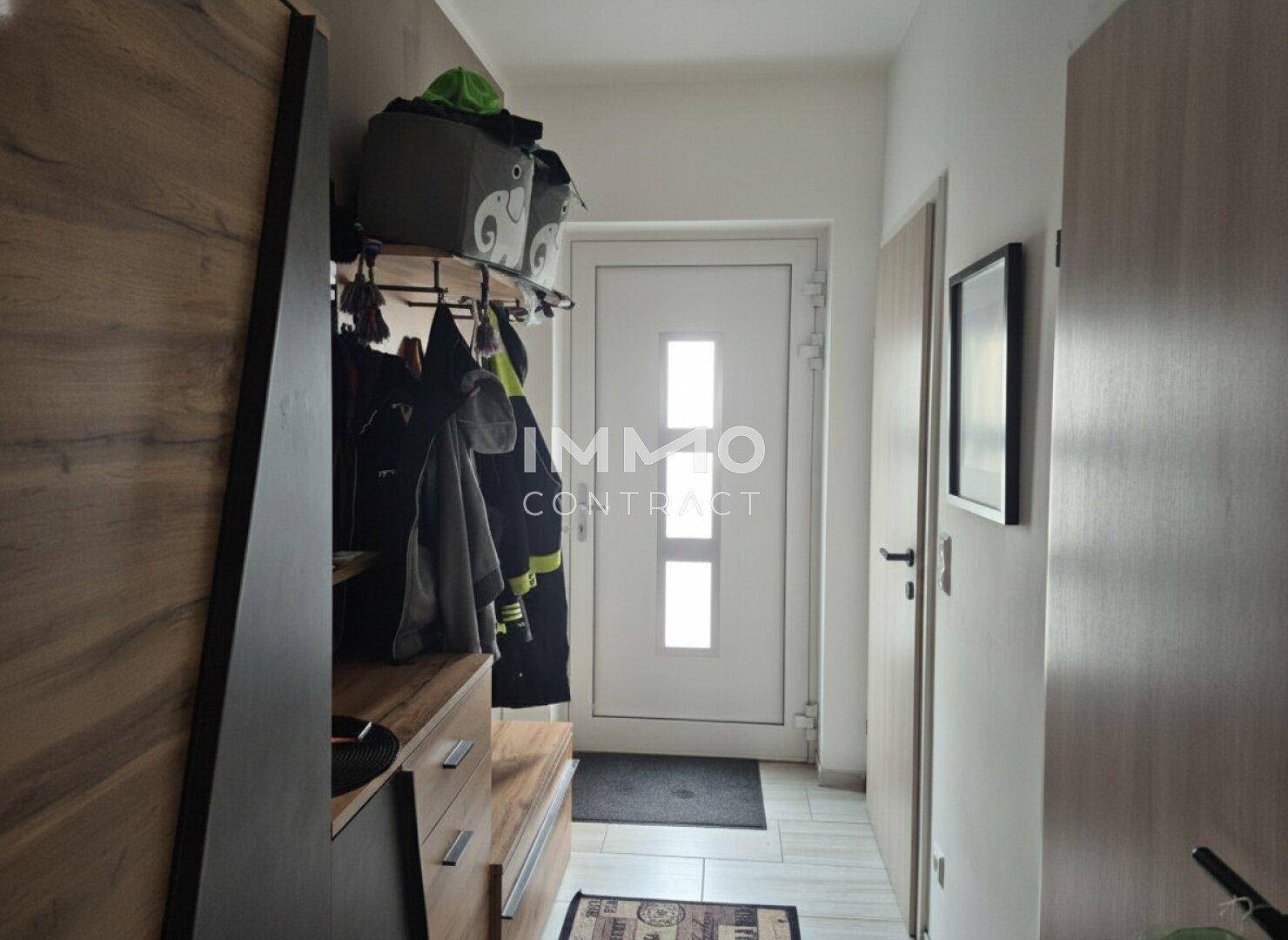 Heller Eingangsbereich mit Garderobe, Holzmöbeln und weißer Eingangstür.