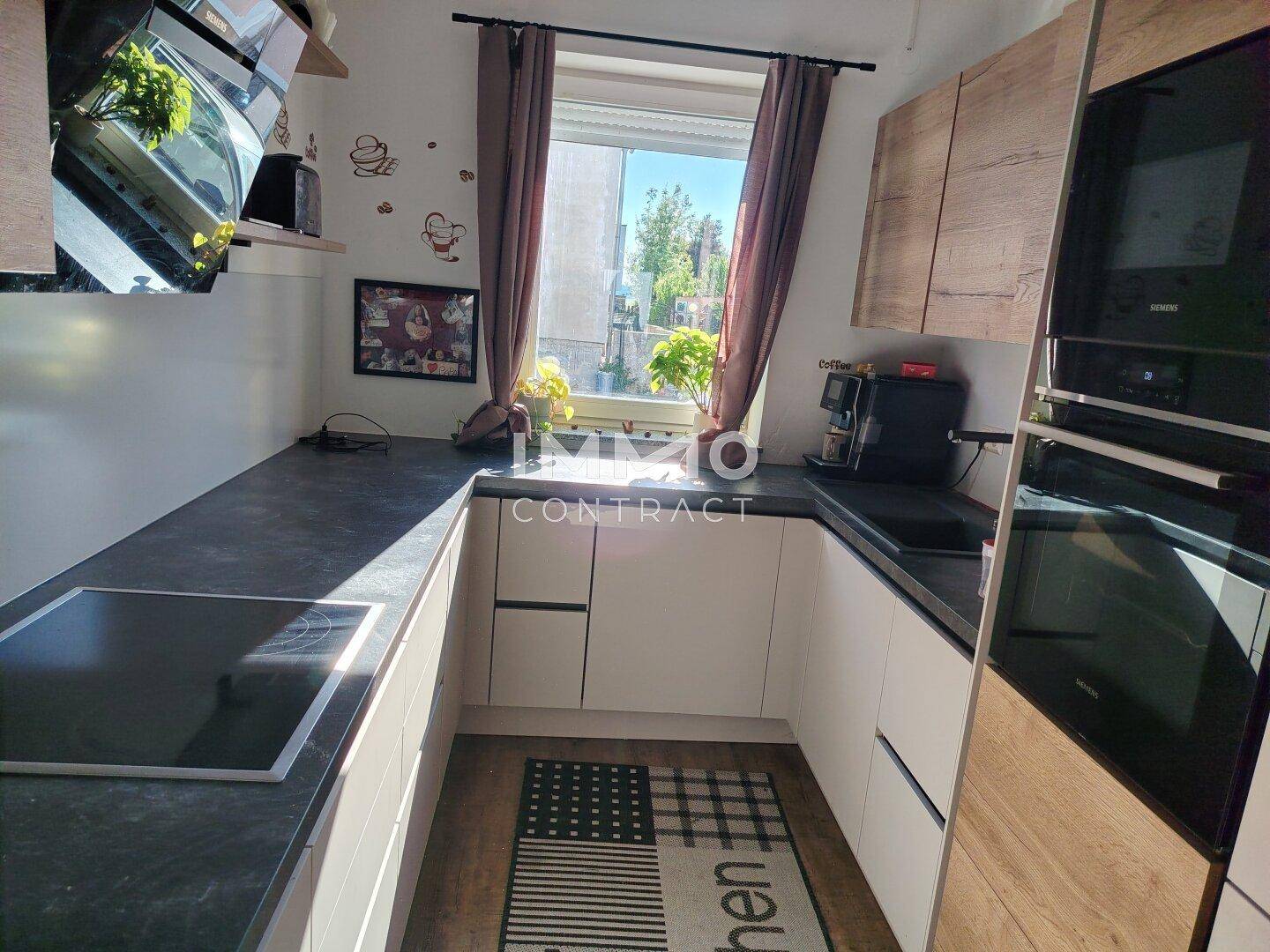 Moderne Küche mit weißen Unterschränken, dunkler Arbeitsplatte und Fensterblick nach draußen.