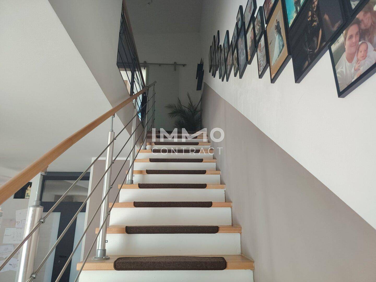 Moderne Treppe mit Holzstufen und Edelstahlgeländer, geschmückt mit Familienfotos.