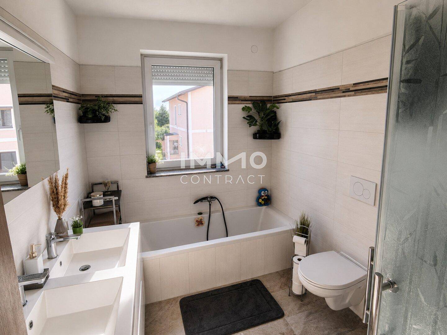 Helles Badezimmer mit Badewanne, Doppelwaschbecken, WC und Fenster.