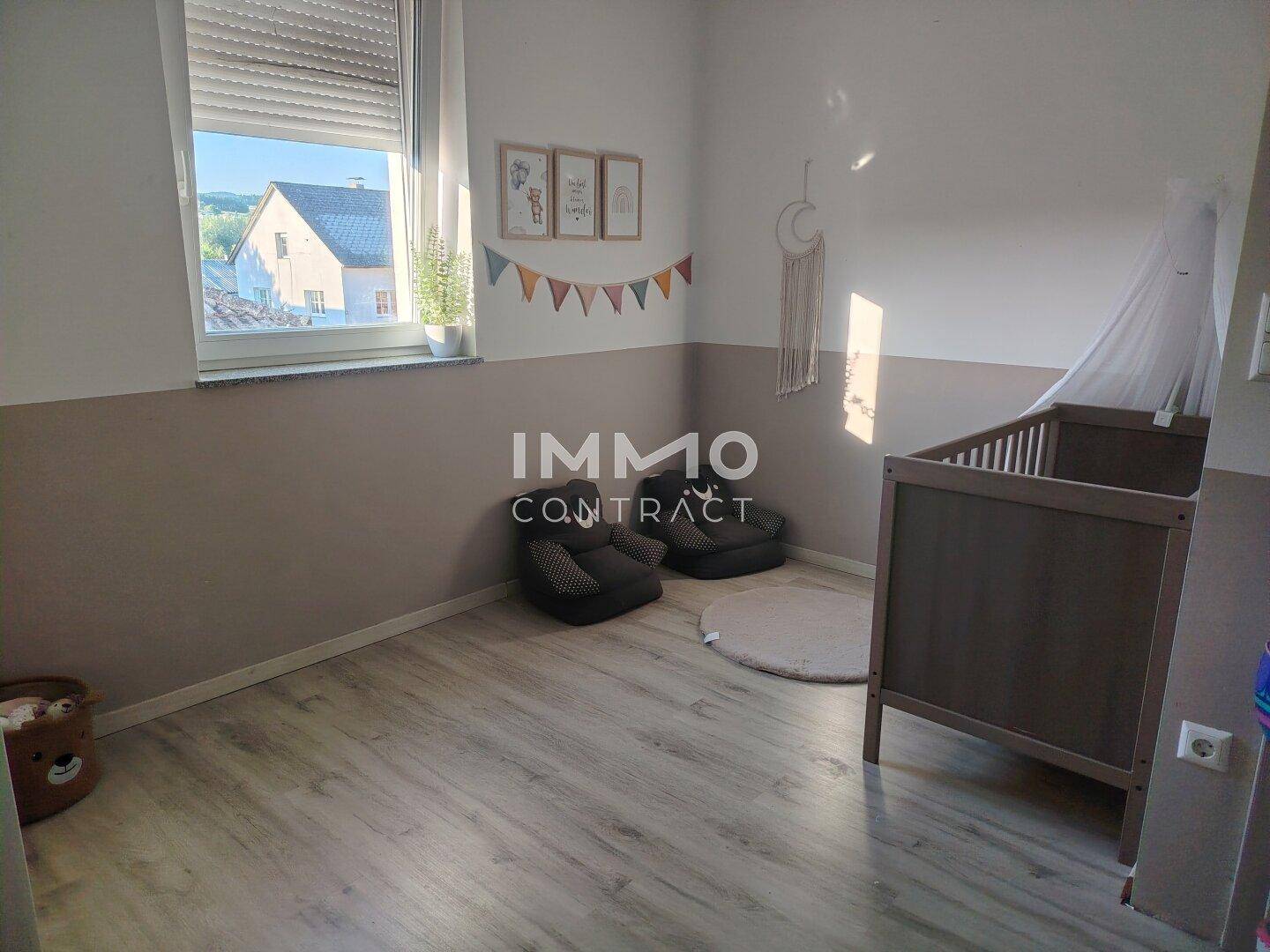 Kinderzimmer mit hellem Laminatboden, Babybett und Fenster mit Rollladen.