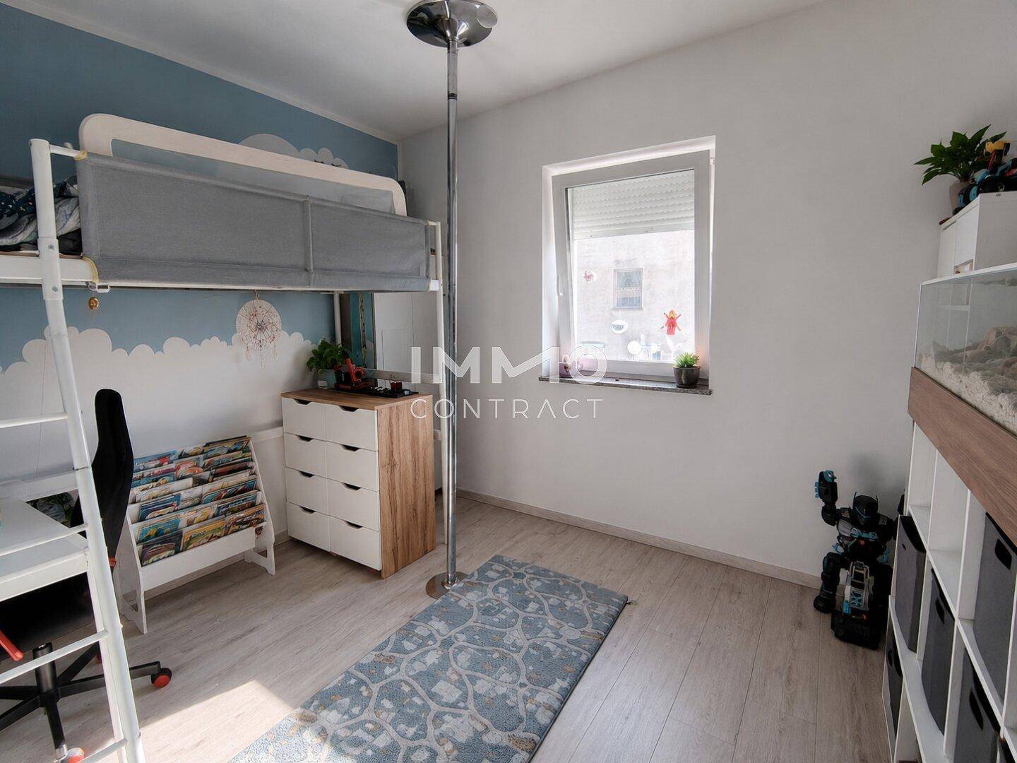 Kinderzimmer mit Hochbett, Schreibtisch und Fenster mit Blick nach draußen.