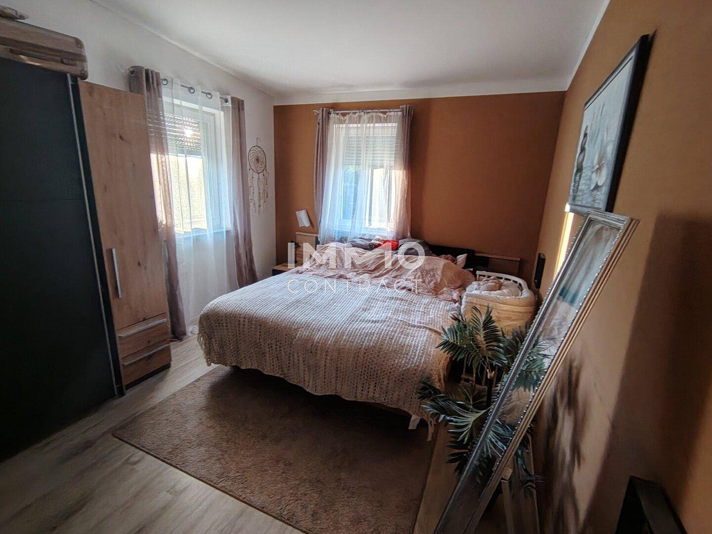 Gemütliches Schlafzimmer mit Doppelbett, Kleiderschrank und zwei Fenstern.
