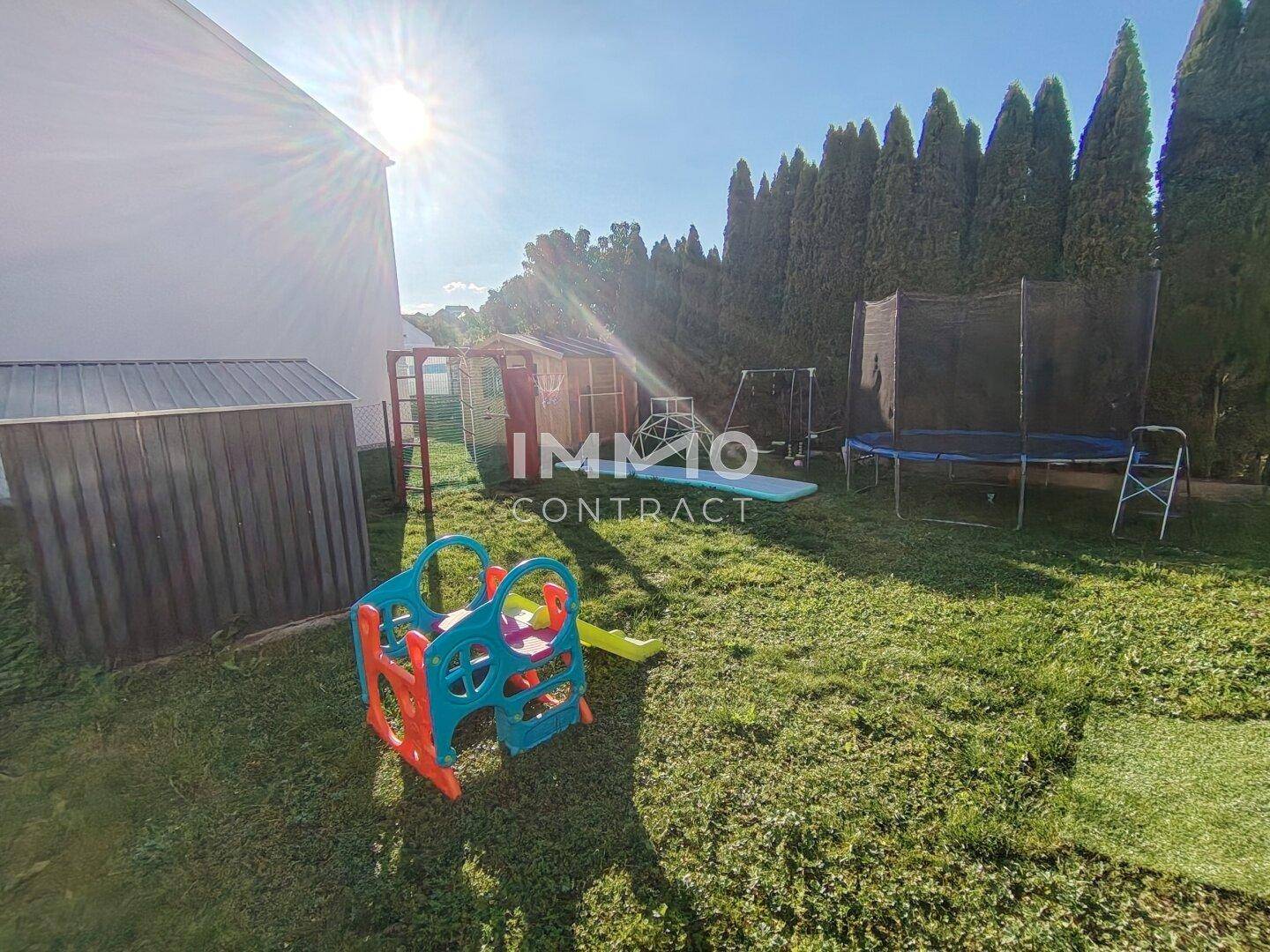 Großer Garten mit Rasenfläche, Trampolin und Kinderspielgeräten unter blauem Himmel.
