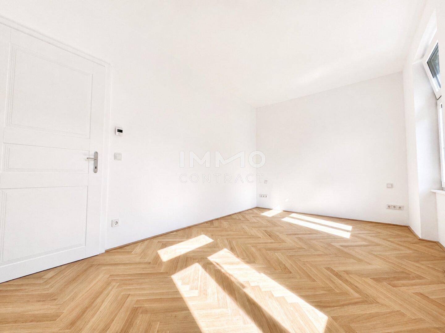 Unmöbliertes Zimmer mit Fischgrätparkett und sonnigem Lichteinfall durch das Fenster.