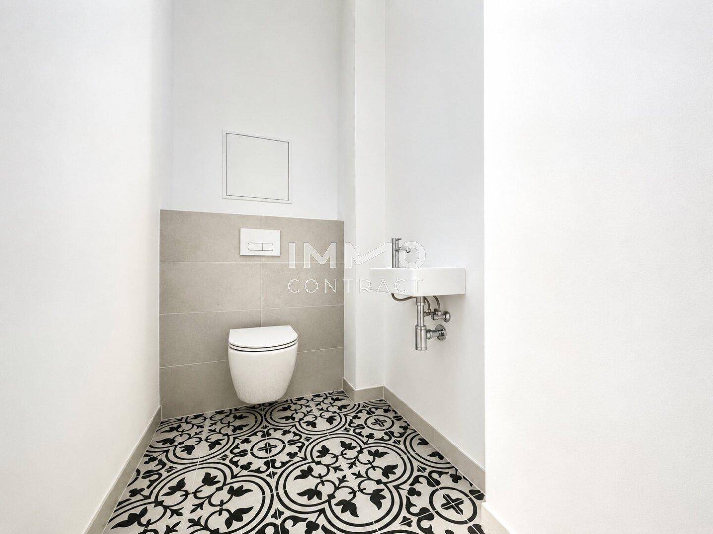 Gäste-WC mit Wand-WC, kleinem Waschbecken und auffälligen gemusterten Bodenfliesen.