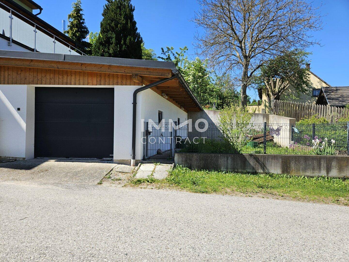 Außenansicht der Garage mit schwarzem Tor und angrenzendem kleinen Gartenbereich.