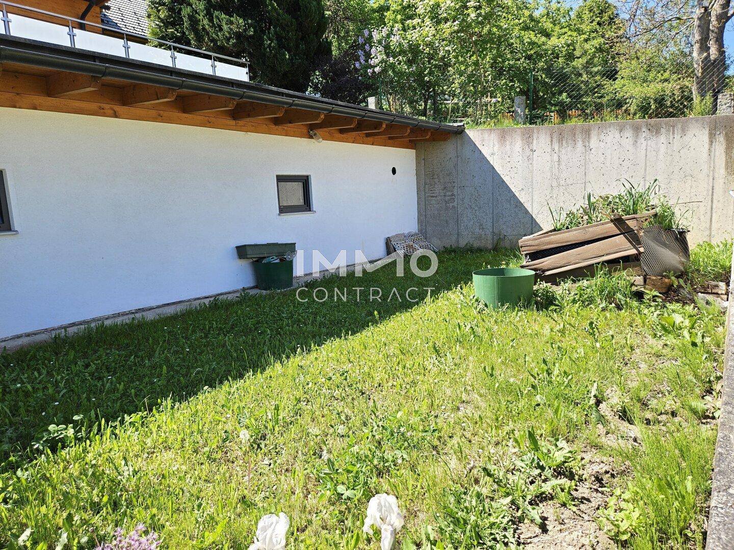 Kleiner Gartenbereich mit Rasenfläche und Betonmauer neben dem Gebäude an einem sonnigen Tag.