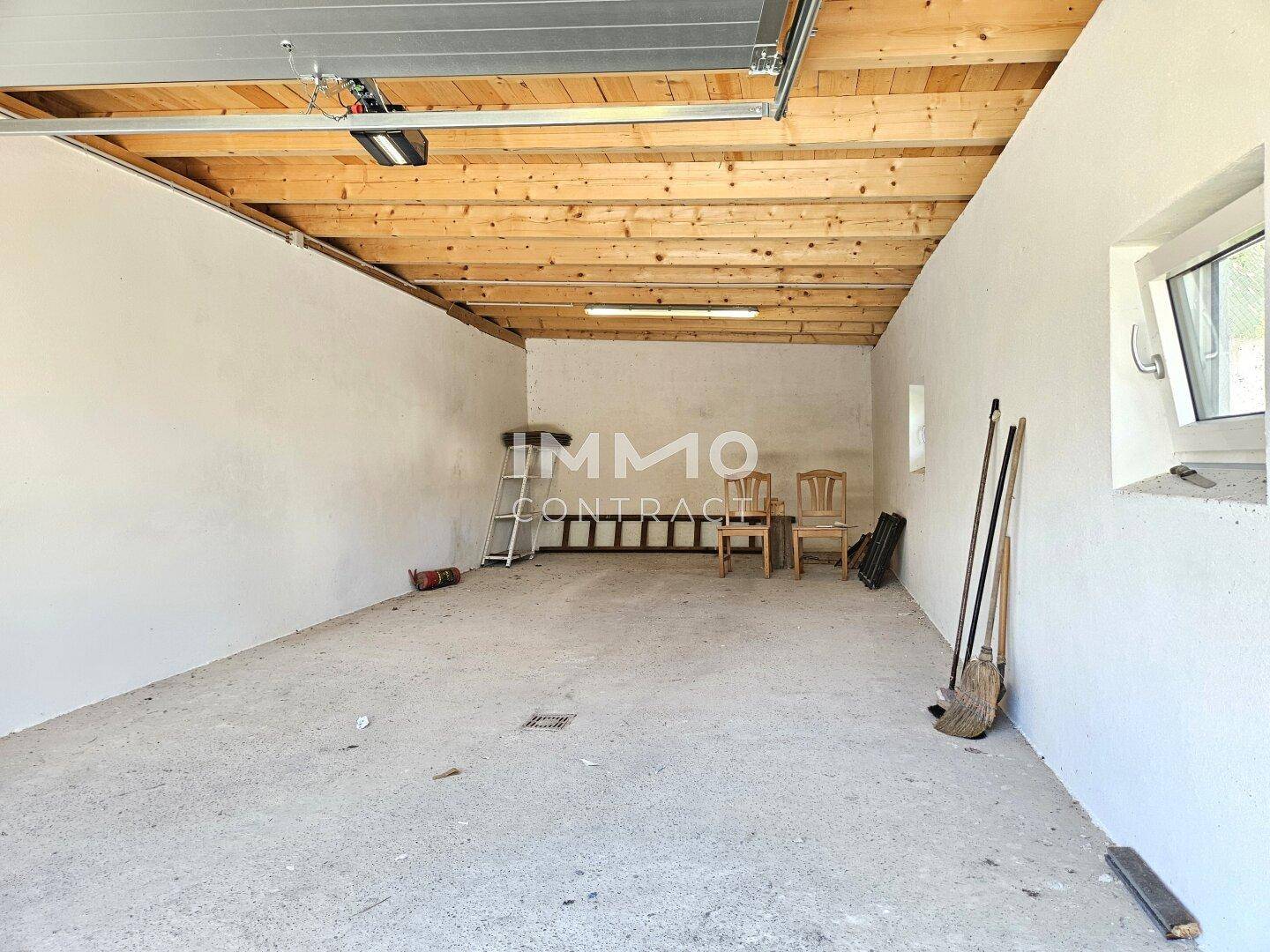 Geräumige Garage mit Betonboden und sichtbaren Holzdeckenbalken, bietet viel Stauraum.