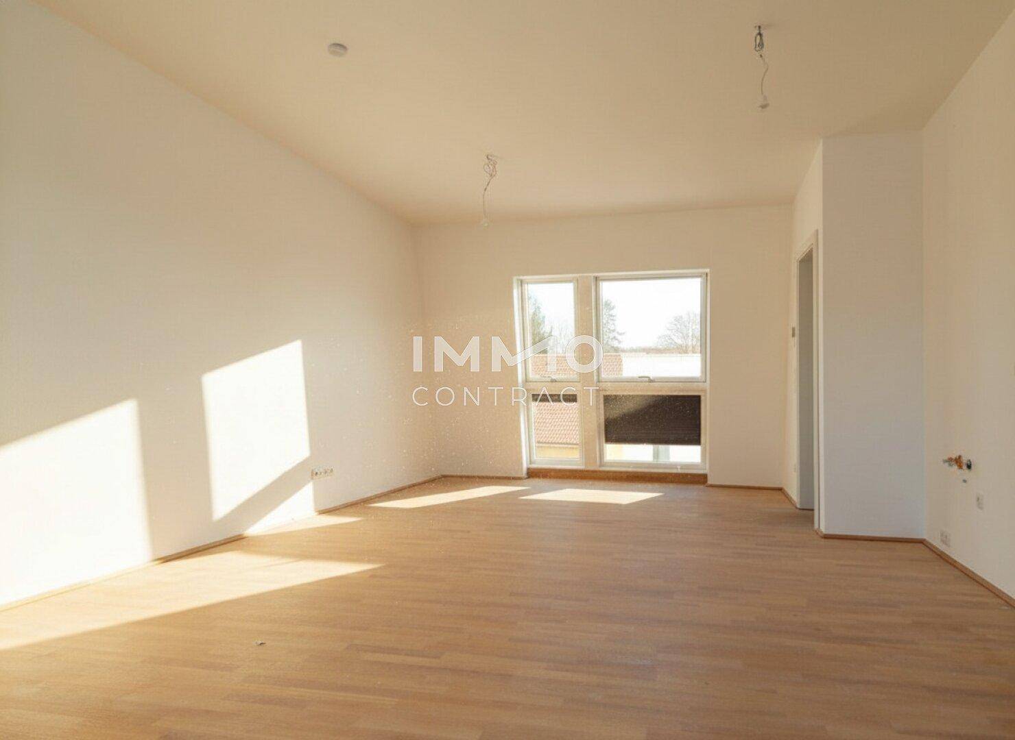 Heller Raum mit Holzboden und großem Fenster, das viel Tageslicht hereinlässt.