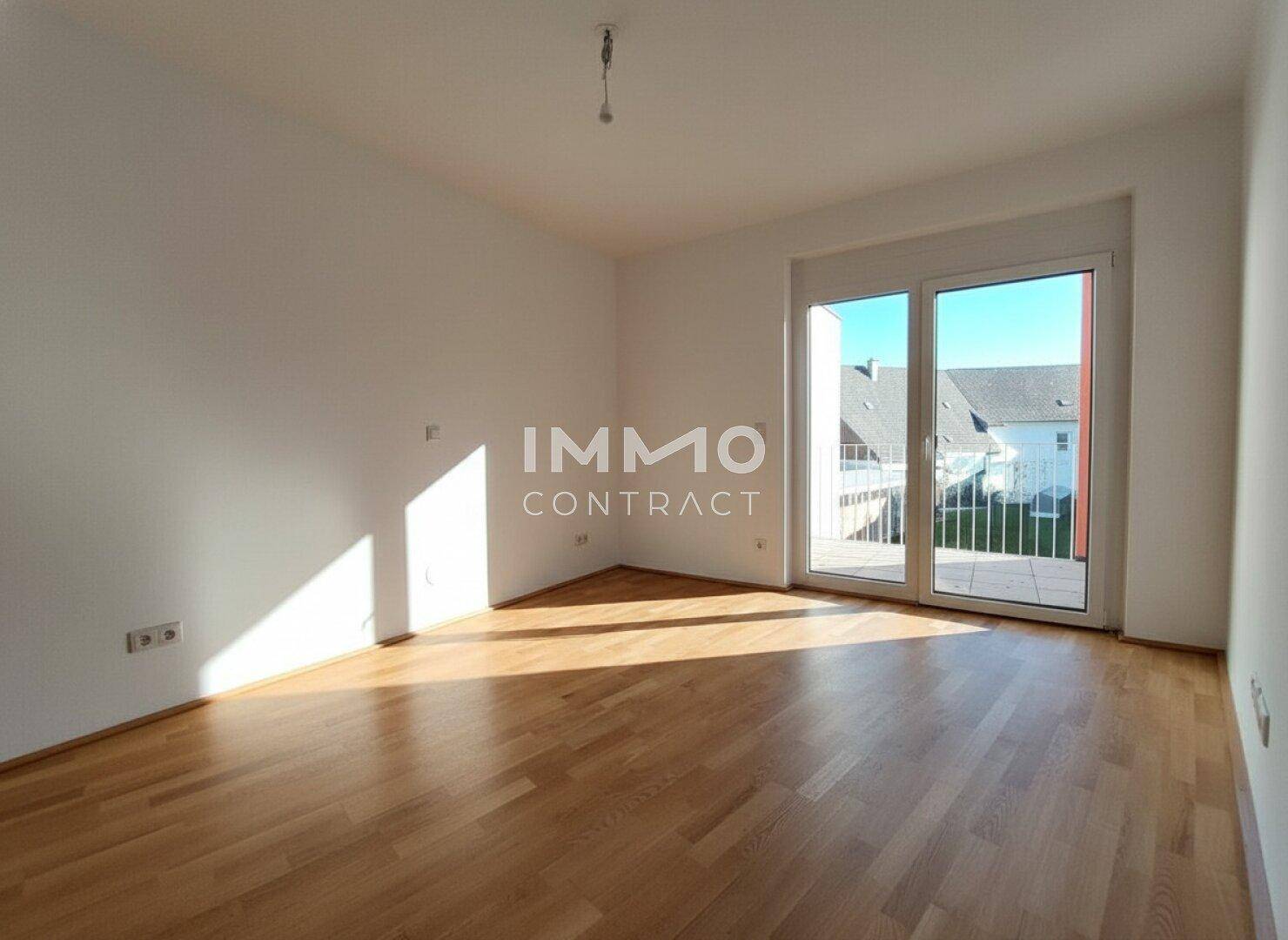 Heller, leerer Raum mit Holzboden und Zugang zu einem Balkon, durchflutet von Sonnenlicht.