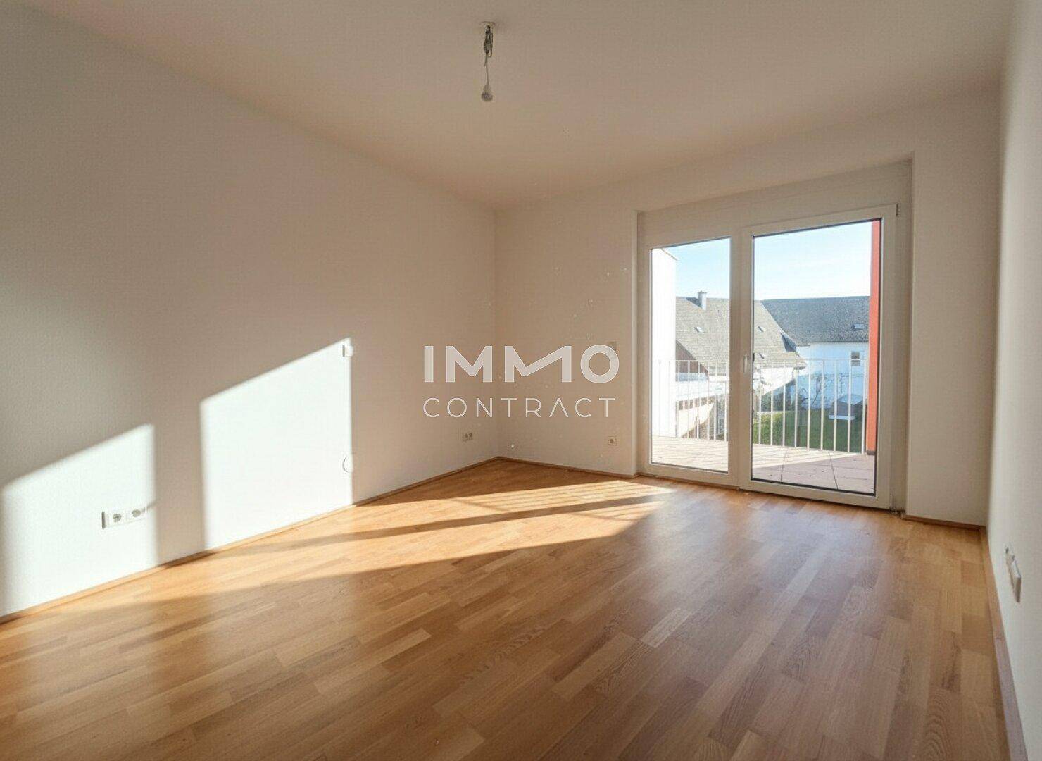 Helles, leeres Wohnzimmer mit Parkettboden, großen Fenstern und Zugang zu einem Balkon.