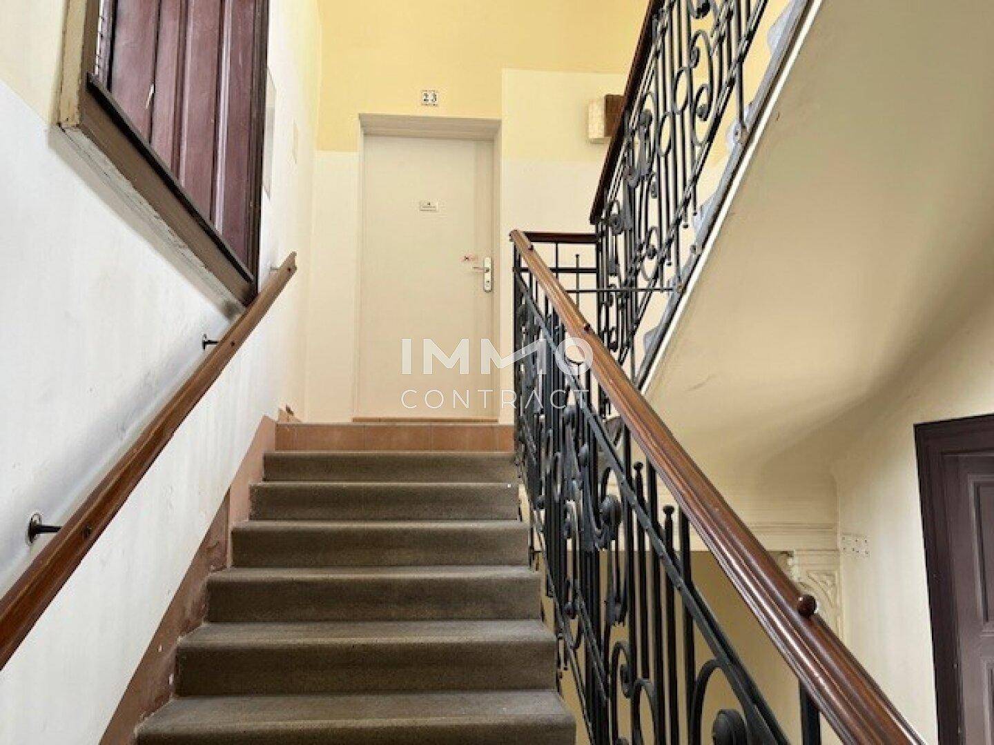Historisches Treppenhaus mit schmiedeeisernem Geländer und Teppichstufen in einem Altbau.