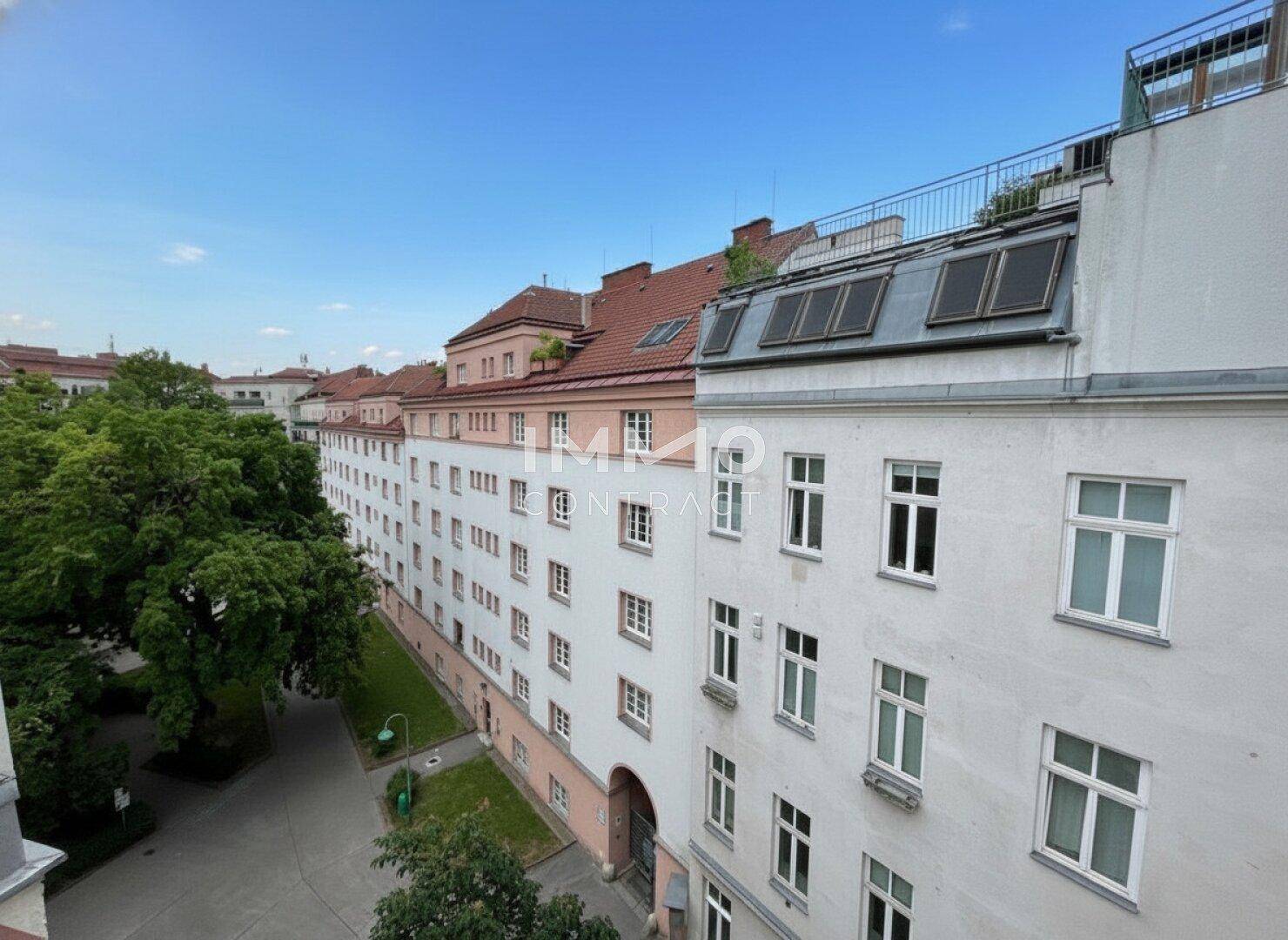 Blick auf die Gebäudefassade eines Altbaus und den begrünten Innenhof mit Bäumen.